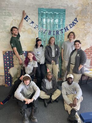SSP's 2023 cohort of Americorps NCCC volunteers helped throw a 'birthday party' to celebrate its first year of operation. Team of 9 young adult NCCC members pictured in front of a Happy Birthday banner. 