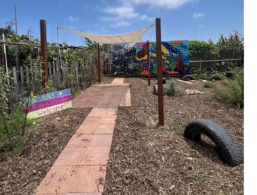 A pathway leads past a "welcome" sign to a shaded awning.