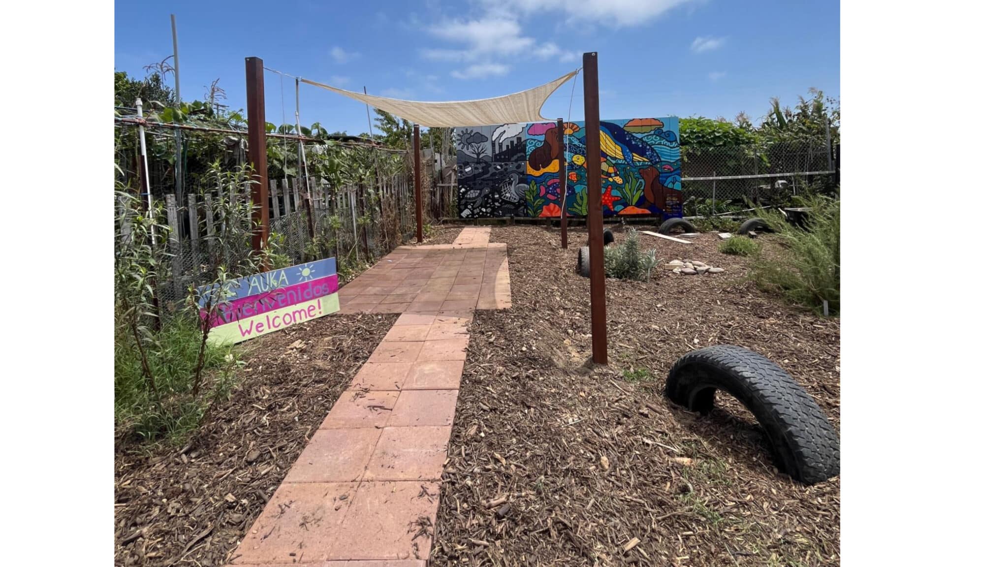 A pathway leads past a "welcome" sign to a shaded awning.